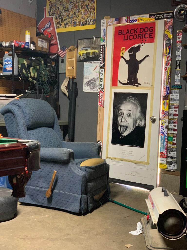 A worn blue recliner beside a door covered in stickers and posters, including Einstein sticking out his tongue