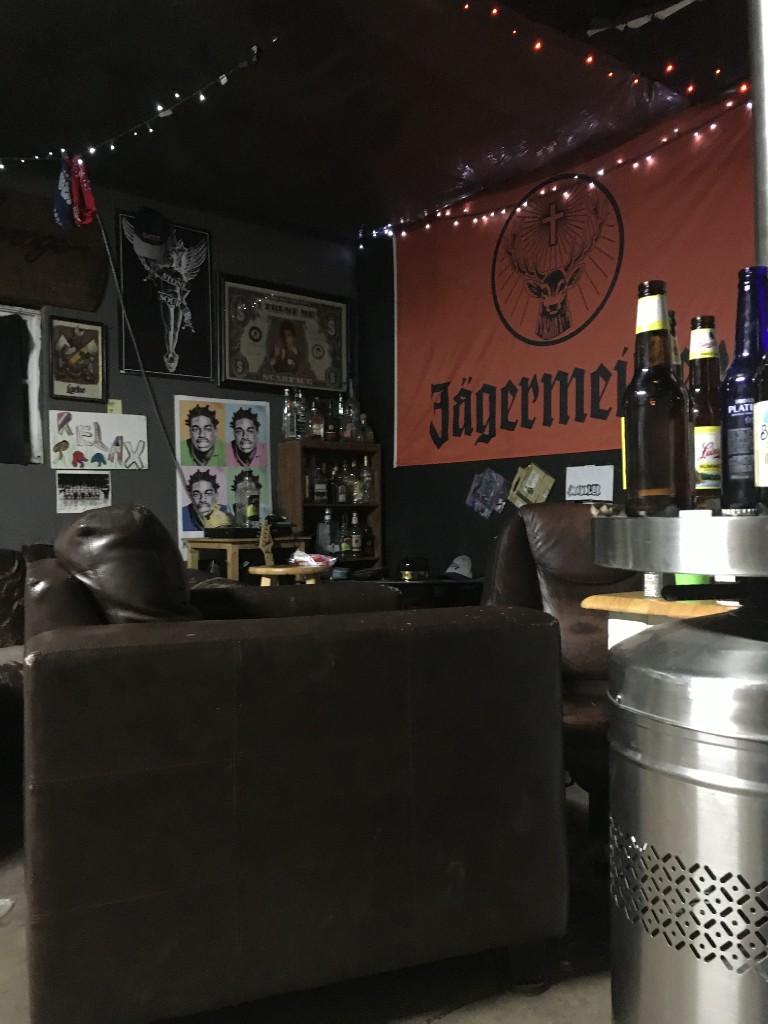The garage at night seen from behind a leather couch, with bottles on a table and the Jägermeister banner on the wall