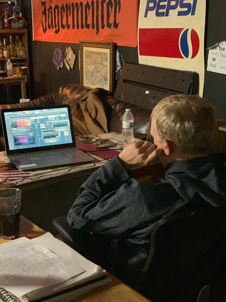 Jarrett at a laptop working on a mix, with a notebook of handwritten lyrics on the table beside him
