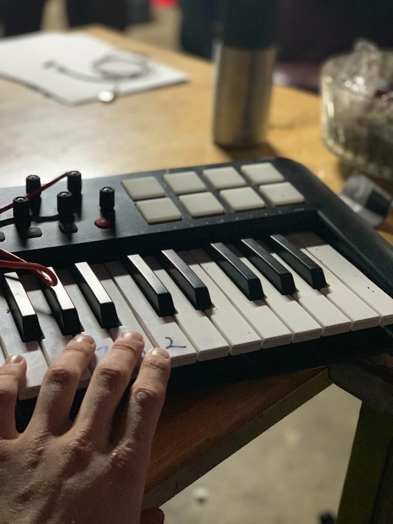 A hand resting on a small MIDI keyboard with drum pads on a wooden table