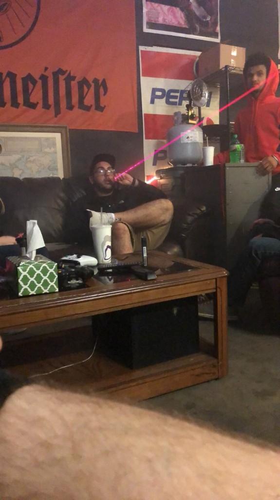 Friends on a couch in the garage at night with a pink laser beam crossing the room