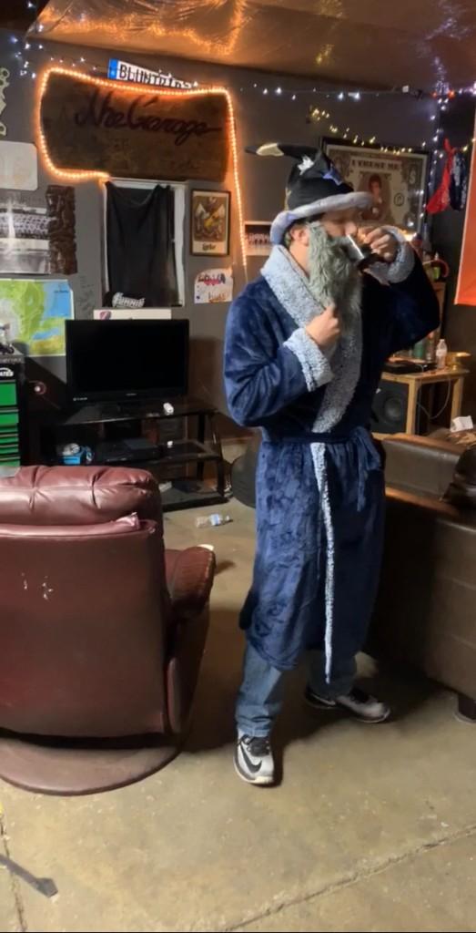 A friend in a wizard costume with a fake gray beard drinking from a mug in the garage